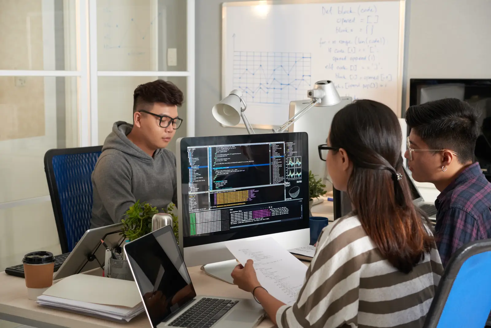 young-woman-checking-programming-code-computer-screen-comparing-with-code-printed-document (1)